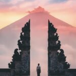 Serene sunrise view of a person standing at Lempuyang Temple's gateway, Bali, Indonesia.
